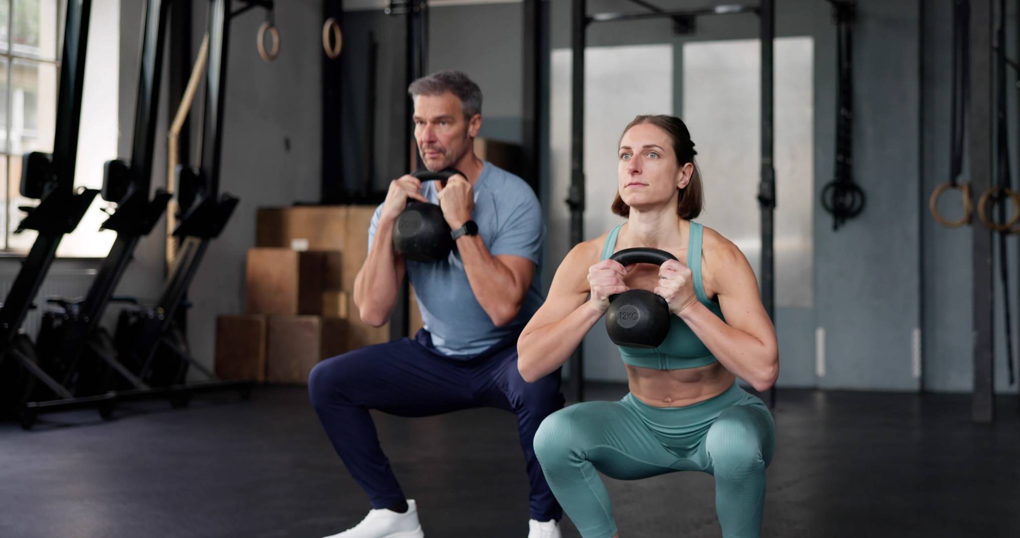 Fit couple performing goblet squats with kettlebells